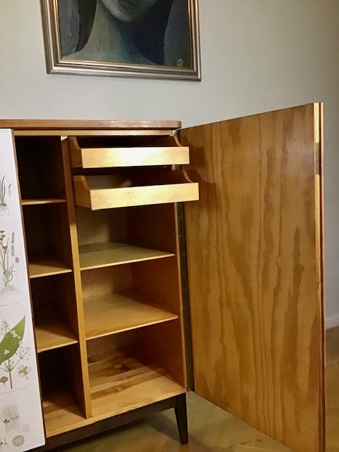 Wooden cabinet with open door and drawer, wall art in the background