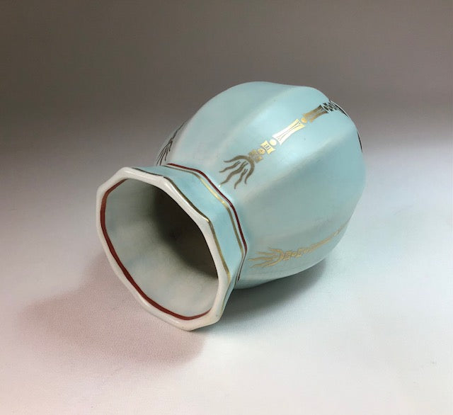 Light blue ceramic vase with gold decorative elements on a gradient background