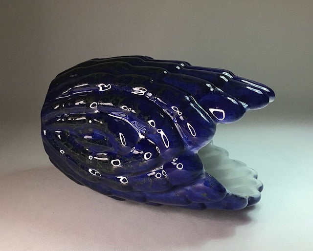 Blue glass sculpture on a white surface with a gray background