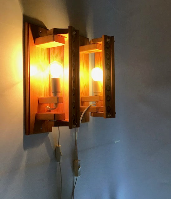 Wooden wall sconce with two lit bulbs on a light gray wall.
