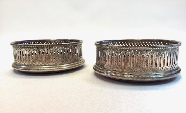 Two silver metal coasters with decorative perforated design on a white background